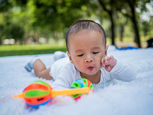 Young baby doing tummy time reaching for a toy