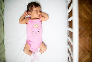 Baby girl lying on her back with just a sheet under her and nothing else in the crib with the her.