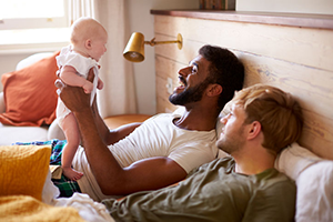 Two fathers enjoying time in bed with their new baby.