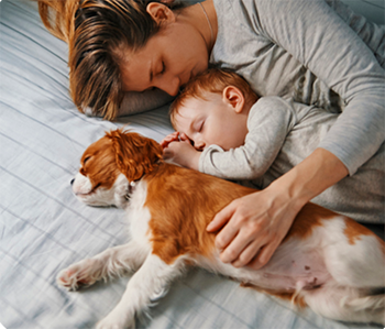 A baby sleeping between his mom and a puppy which is not recommended for a SafeSleep360° environment.