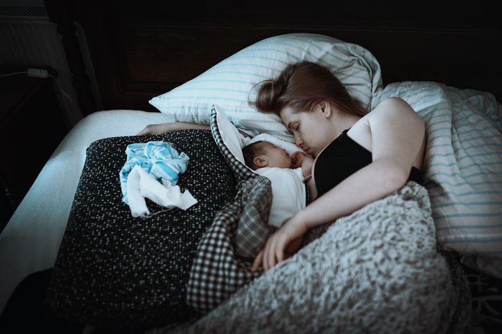 A baby sleeping between her mom and a bulky quilt.